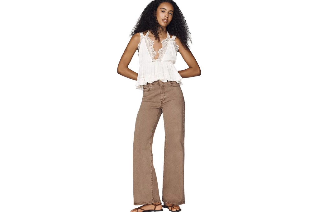 A model wearing a white lace-trimmed top paired with brown flared jeans.