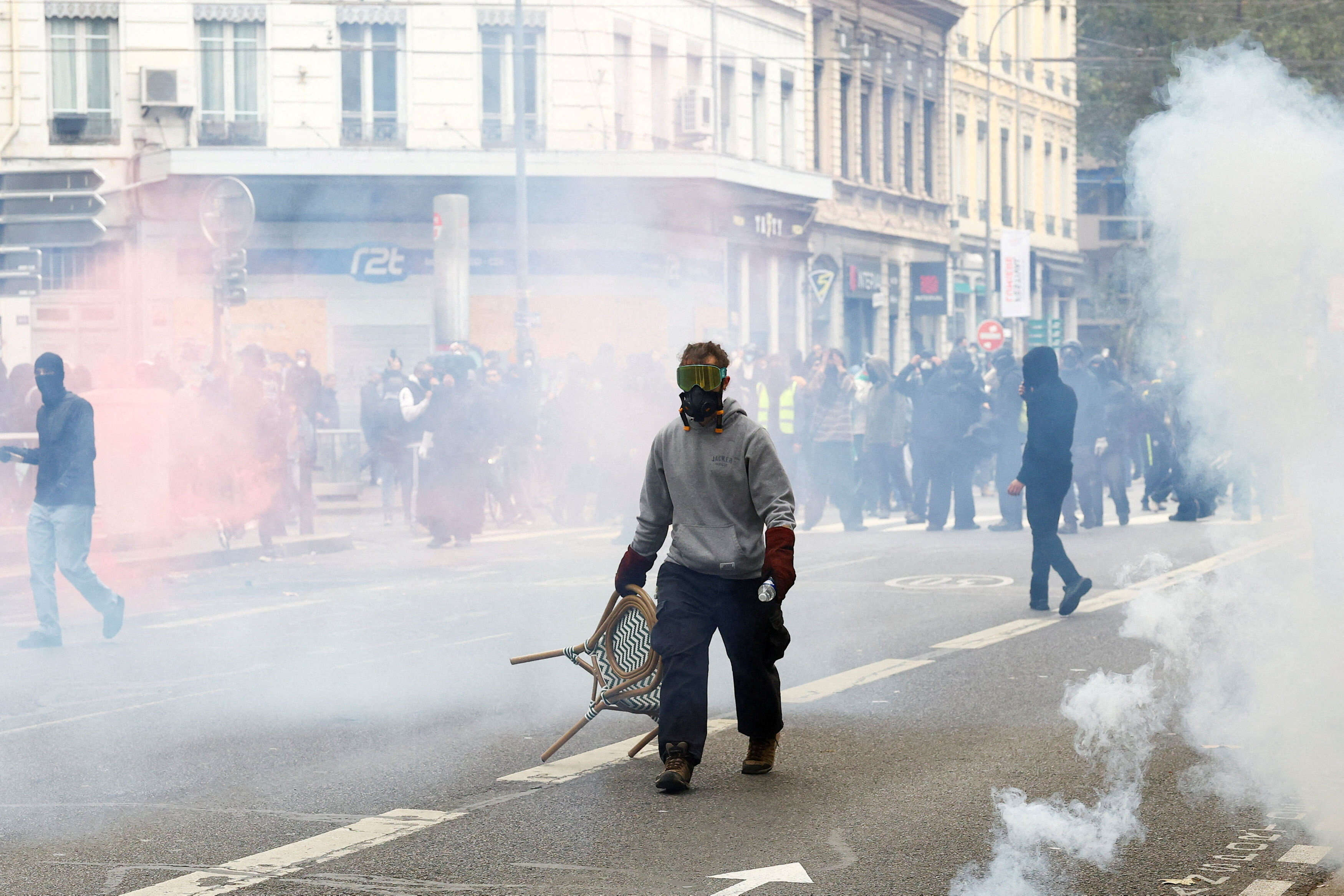 A protester, wearing a gas mask and protective eyewear, drags a chair amidst tear gas, during a demonstration banned by local authorities and called by the "Yellow Vests" movement. Second nationwide day of protests against the cost of living in France