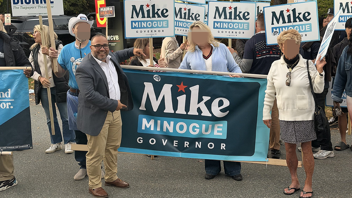Shawn Oliver stands beside supporters holding Mike Minogue campaign signs and a large banner