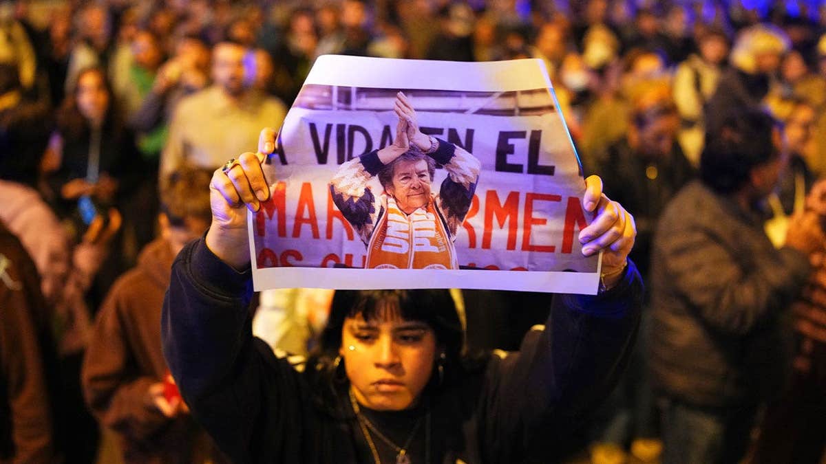 A demonstrator holds a photograph of María del Carmen Abascal during a nighttime protest in Madrid, Spain, following the death of the 87-year-old woman who was evicted from her home of 70 years