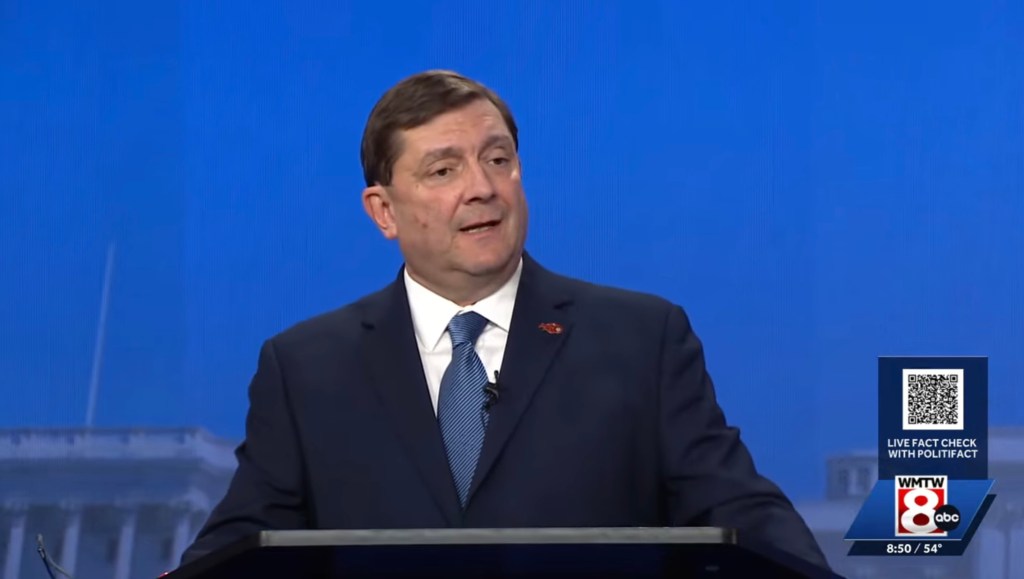 Troy Jackson speaking at a podium against a blue backdrop.