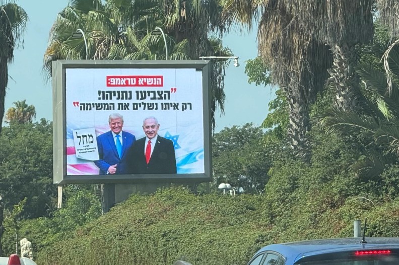 Donald Trump and Benjamin Netanyahu appear on a roadside billboard with Hebrew campaign text amid palm trees.
