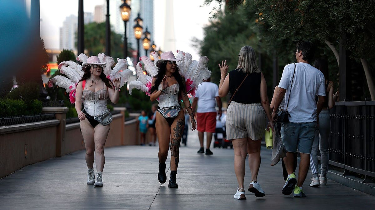 Women dressed as showgirls wave to visitors along the Las Vegas Strip.