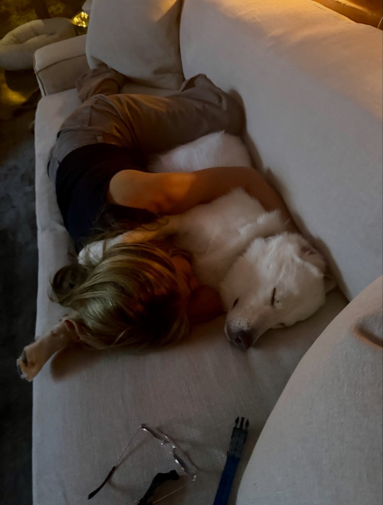 Jennifer Aniston cuddling and sleeping on a white couch with her white dog.